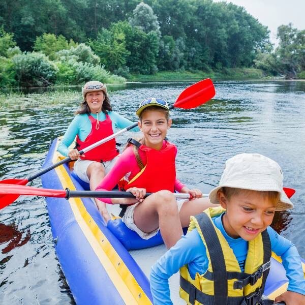 A mom and two young sons having fun while kayaking on a river.